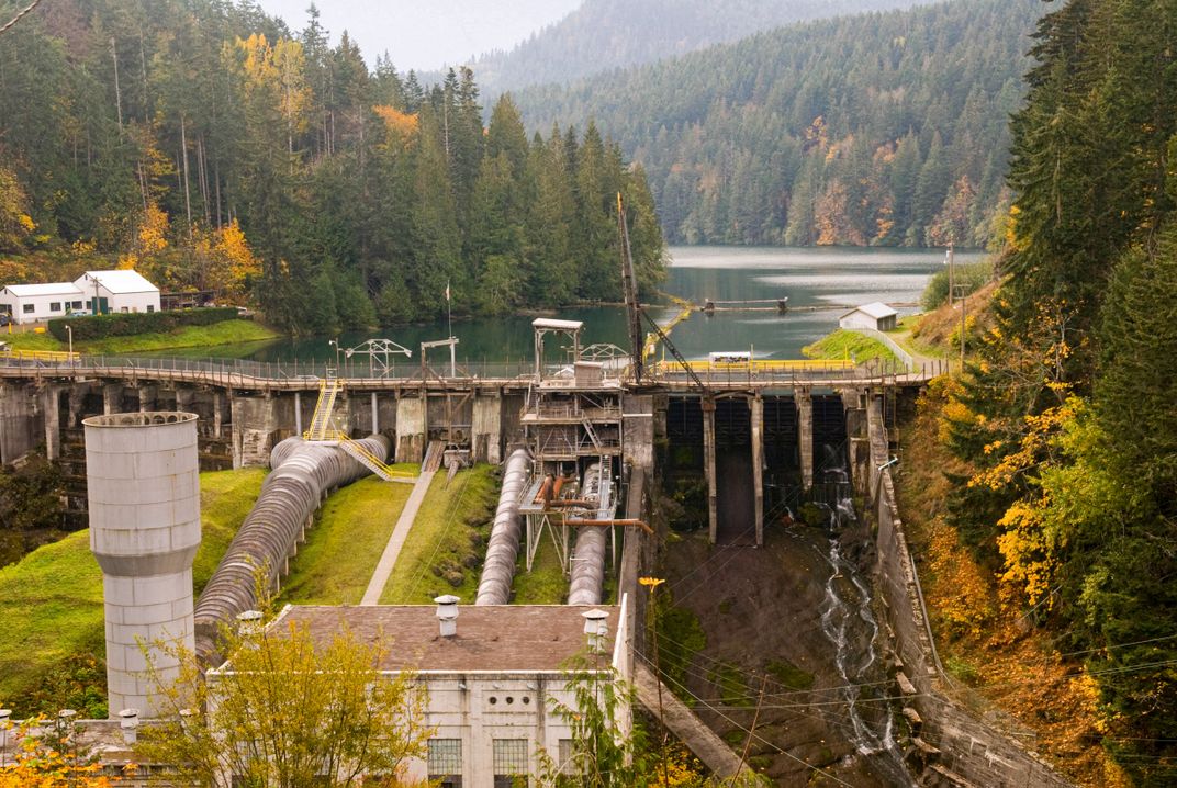 A dam on a river in a forest with a building in the front