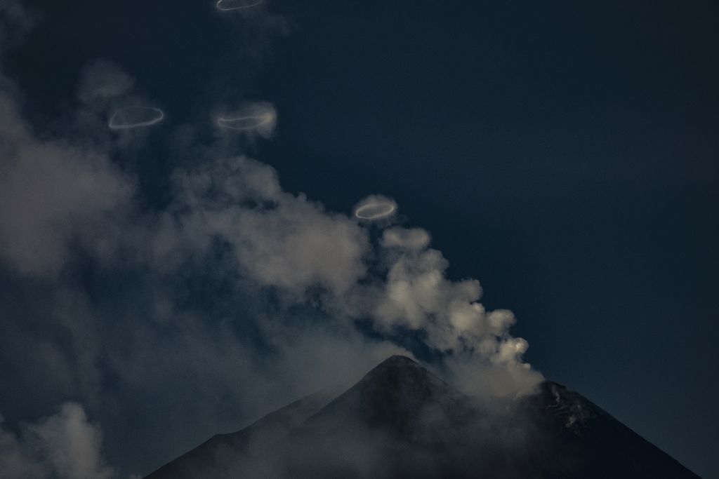 A volcano with wisps of clouds and rings floating above