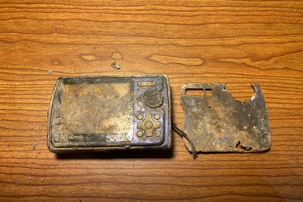 Mud-covered, broken digital camera on a wooden surface