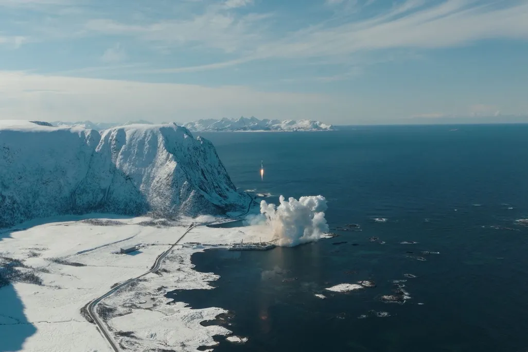 a bird's eye view of a rocket launching near a body of water