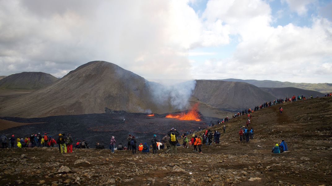 Dozens of spectators in winter jackets and hats watch lava flowing from a fissure
