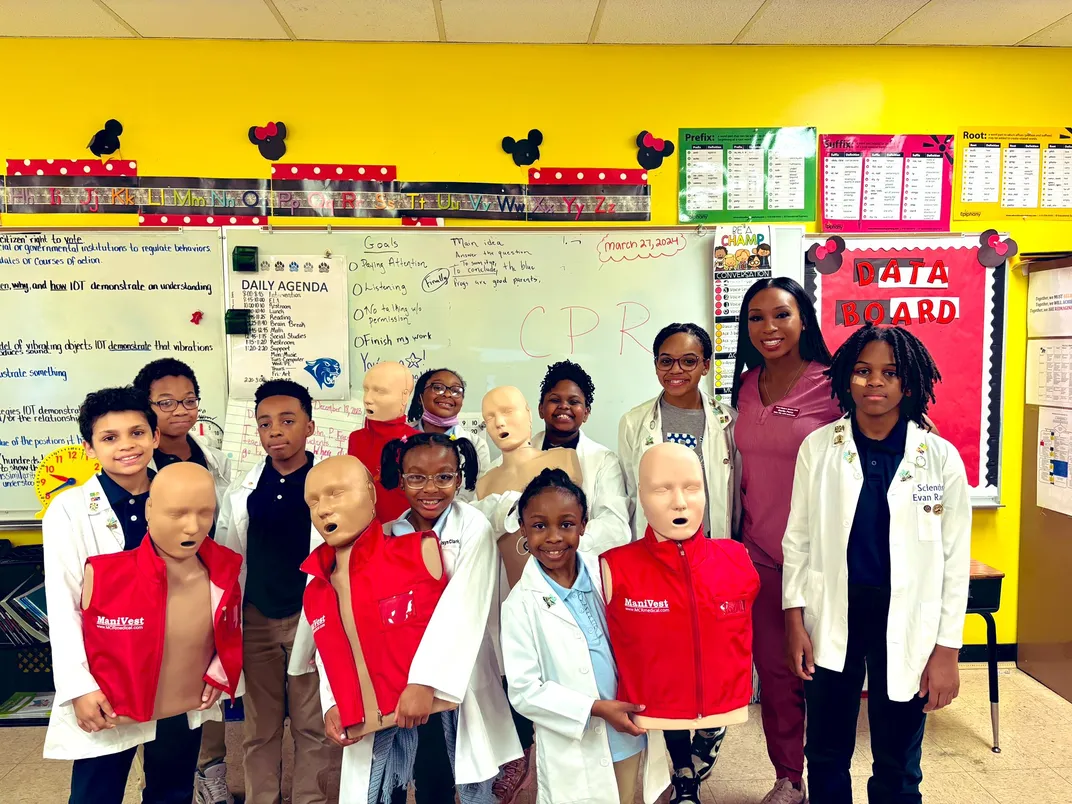 Students in lab coats smile at the camera as they learn about CPR and the medical profession