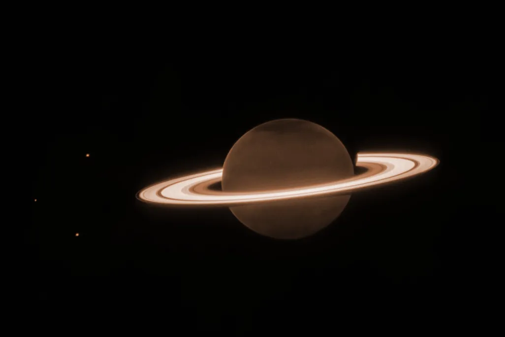 Saturn, with its rings appearing brighter than the planet and three moons to the left of the planet.