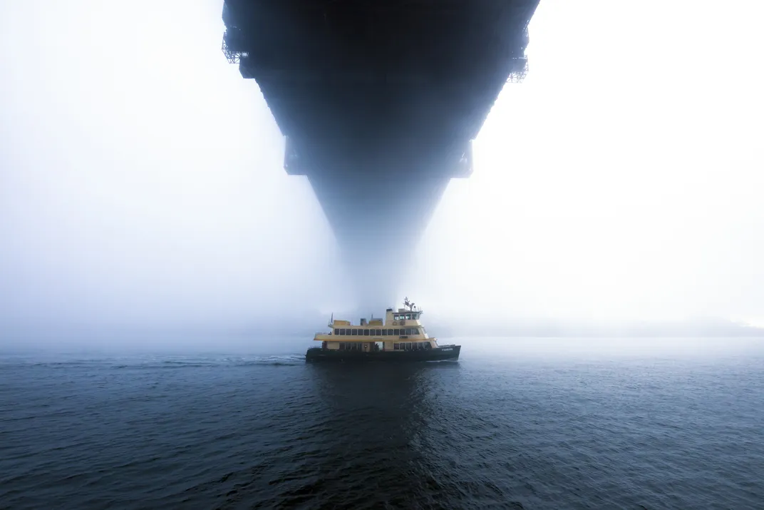 15 - During an early foggy morning in Sydney, a ferry passes through the mist and underneath a harbor bridge.