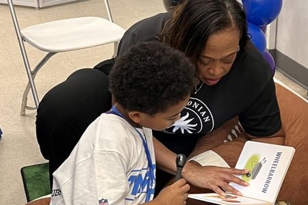 A woman reads with a young boy, the book says "wheelbarrow" in big letters