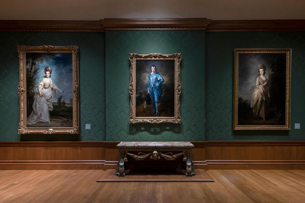 A dark green room with The Blue Boy hanging in the center of the frame and two other portraits on either side of him