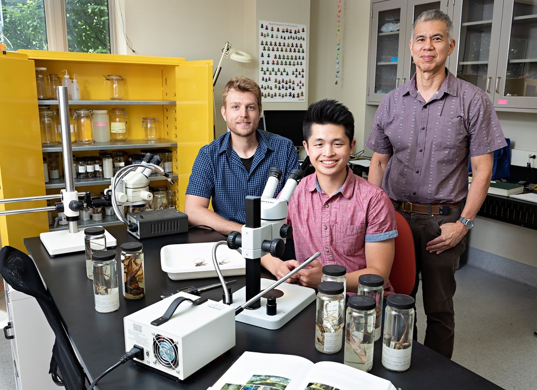 Three scientists at a workbench with a microscope in a lab