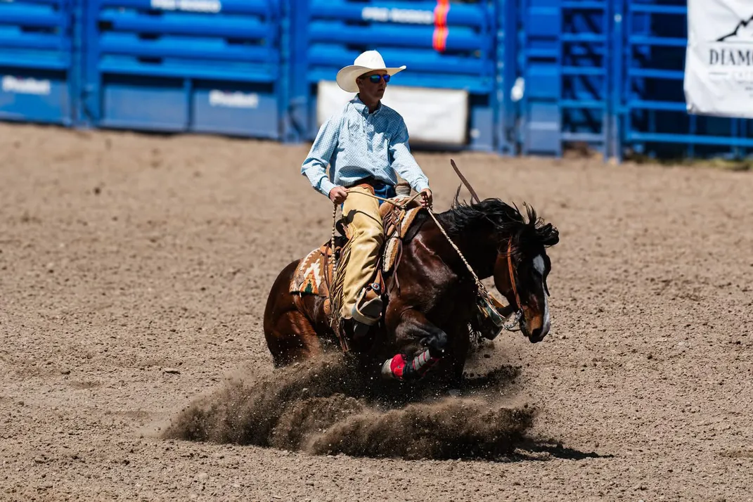 A young man on horseback on a dirt track comes to a halt, the horse kicking up a cloud of dirt.
