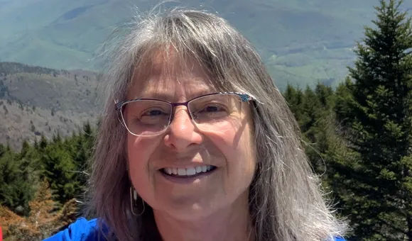 Head and shoulders photo of Denise Breitburg, a woman with glasses and shoulder-length gray hair, with forested mountains in the background.