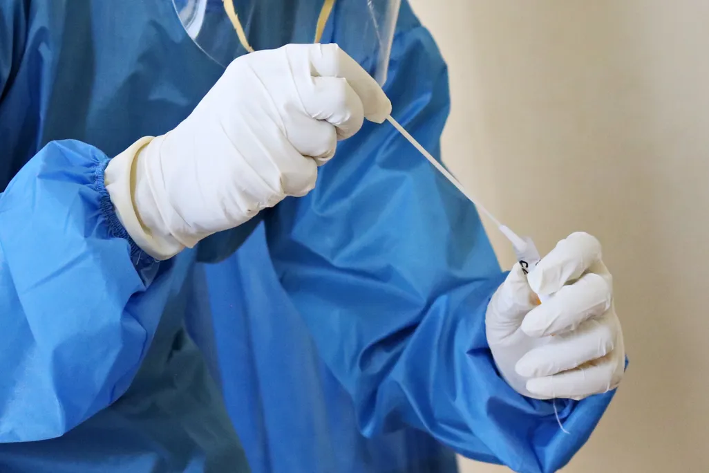 person in PPE holds swab and test tube