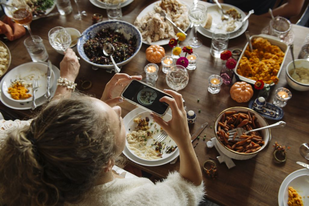 Teenage girl photographing food through smart phone while sitting at dining table during Thanksgiving