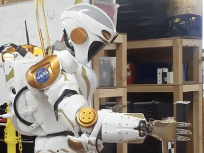 A NASA Valkyrie robot picks up an item with its hand.