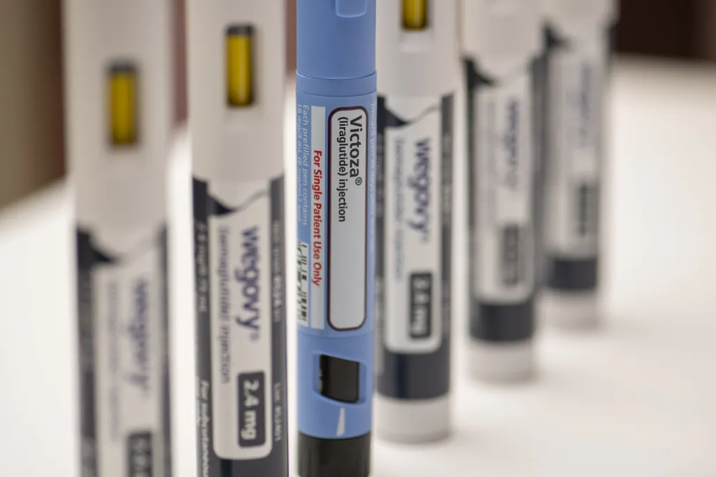 A blue Victoza pen stands in front of blurry, white Wegovy pens