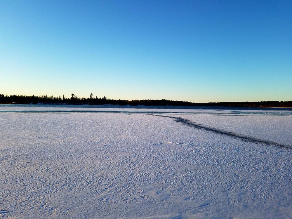 A photograph of a frozen lake landscape with trees on the distant horizon 