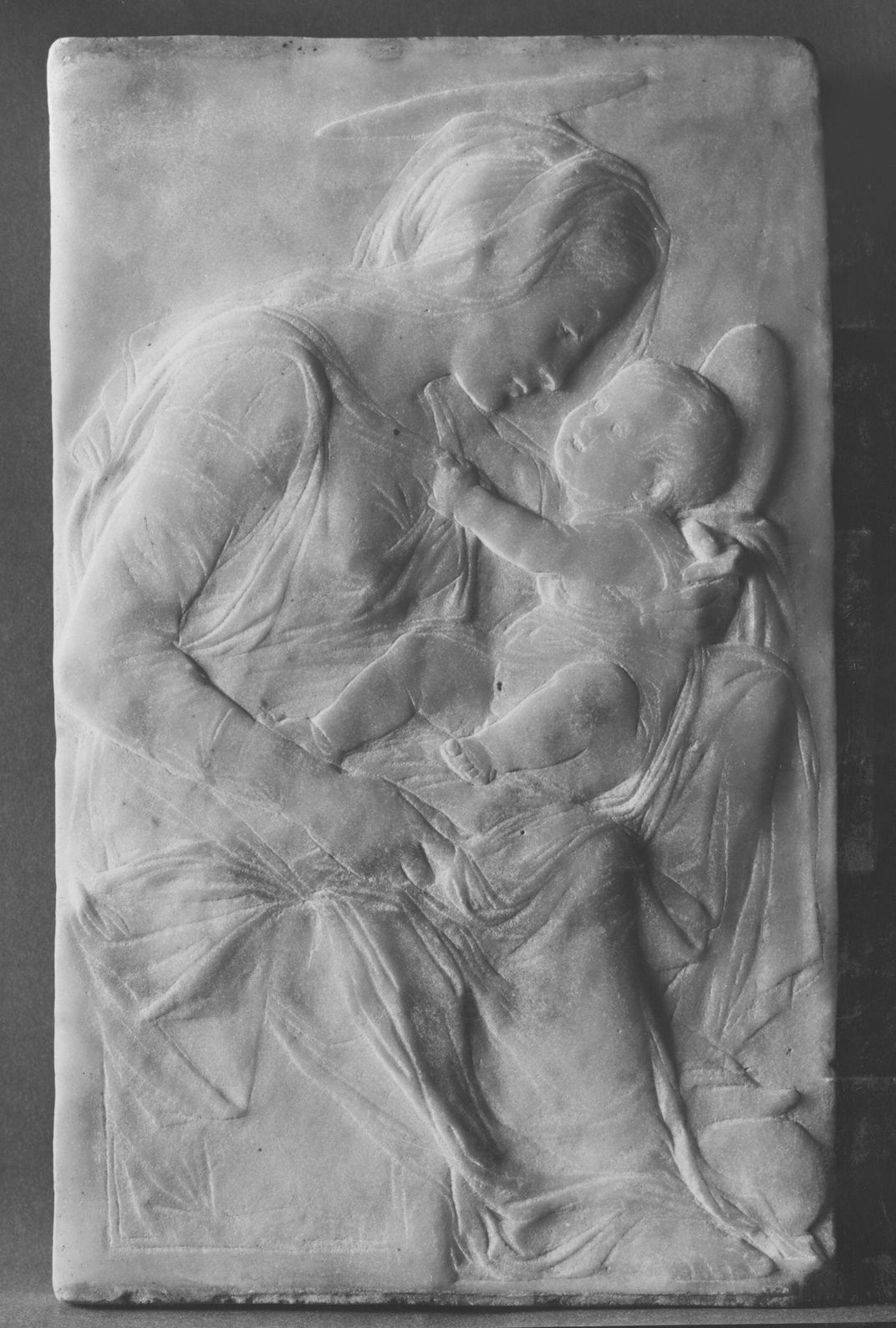 A black and white image of a carved relief of a mother holding a baby with a halo