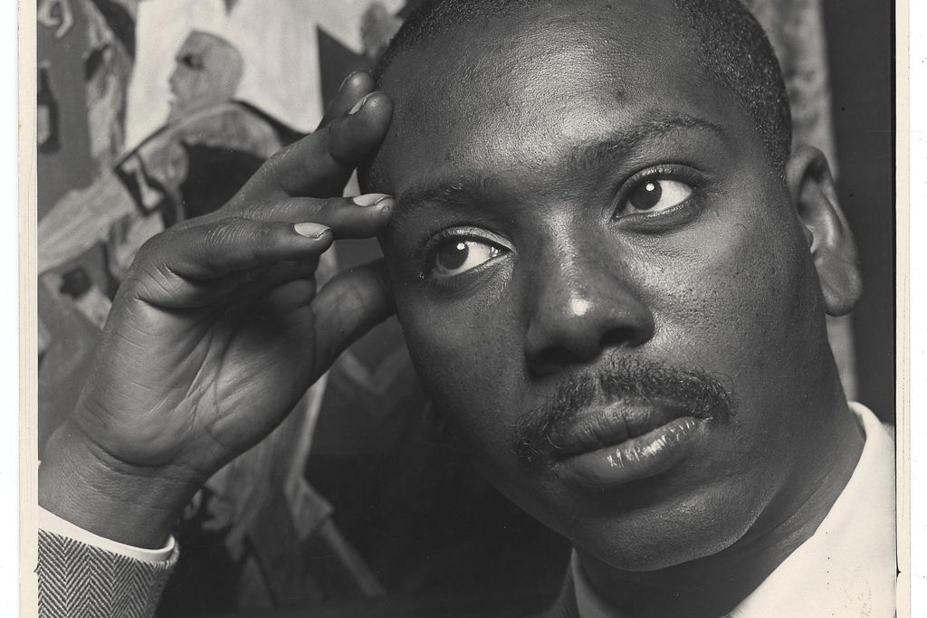 A black and white image of Lawrence, a black man with a mustache, looking contemplative with a suit and tie and resting his head against his hand, in front of one of his works of art