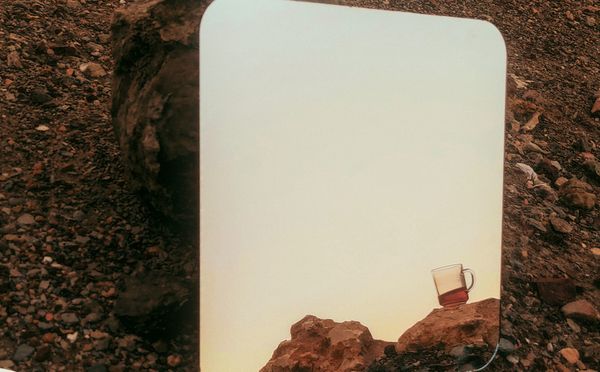 A tea cup out of the blue in the desert mountains in the mirror, conceptual photography. thumbnail