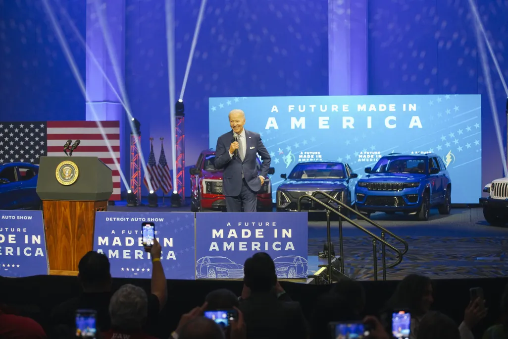President Biden on a stage with cars and signs that read "A future made in America"