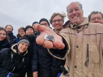 Researchers pose with a fragment of asteroid 2024 BX1 they found in Germany. The rock is a very rare type of meteorite called an aubrite.