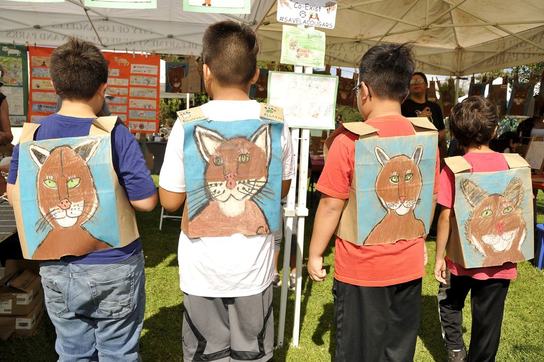 four children face away from the camera to show cougars drawn on paper on their backs