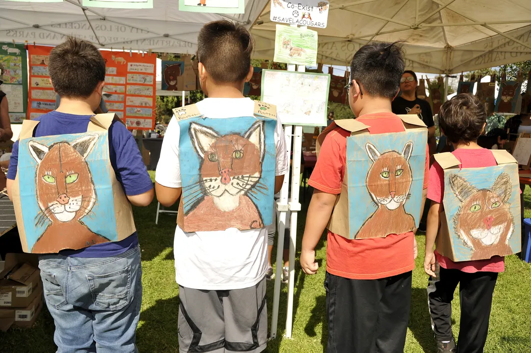 four children face away from the camera to show cougars drawn on paper on their backs