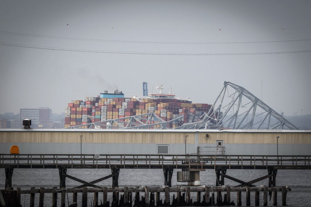 a large container ship in a river with ruins of a truss bridge on top of it
