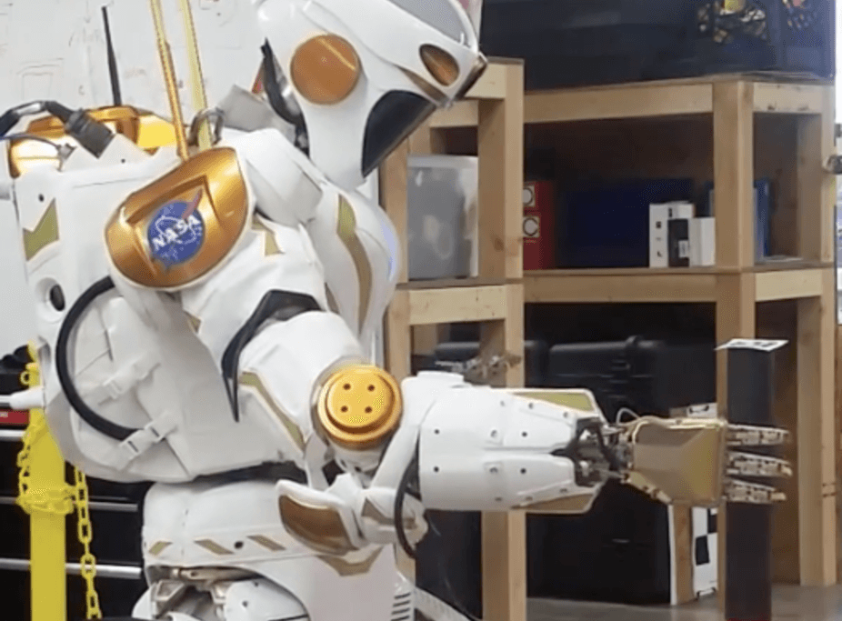 A NASA Valkyrie robot picks up an item with its hand.