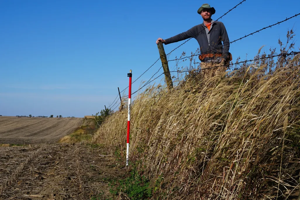 An image of a reseacher standing on native prairie a few feet above degraded farmed land.