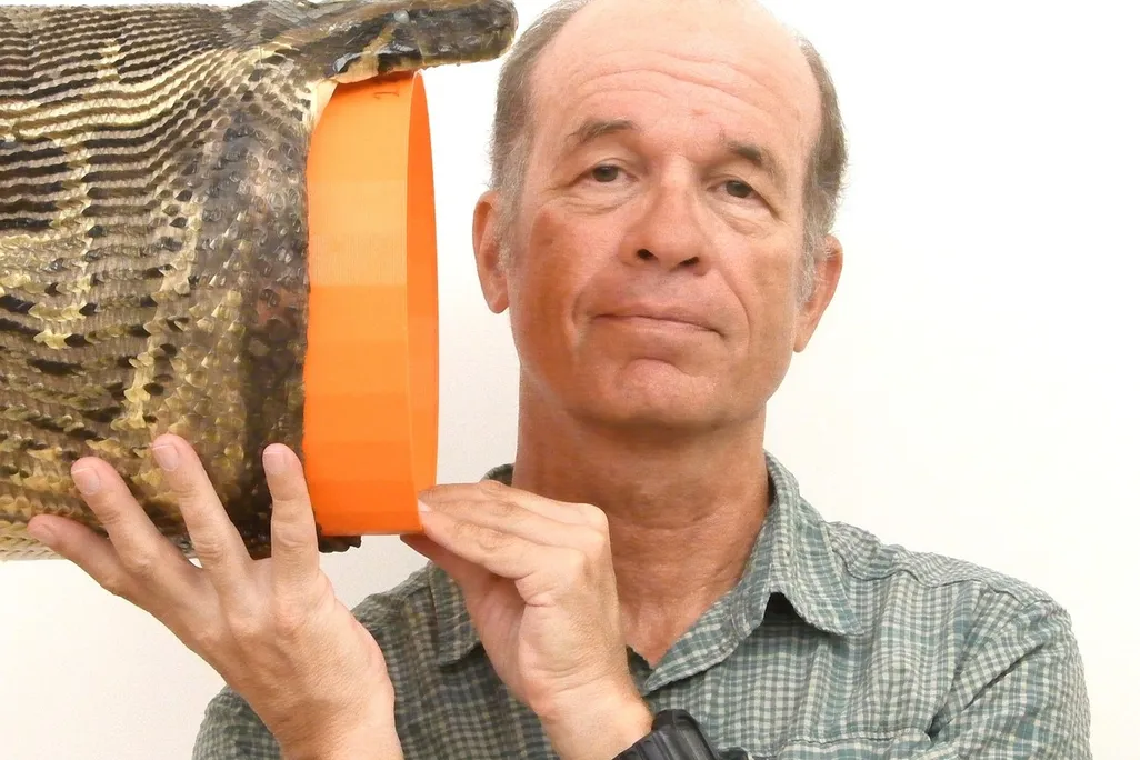 A man holds a snake head with an orange bucket-like object in the mouth