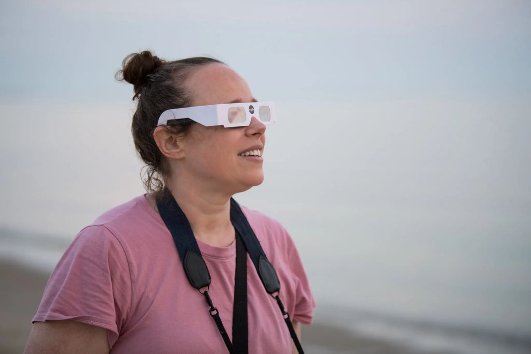 a woman looks toward the horizon with NASA-branded eclipse glasses