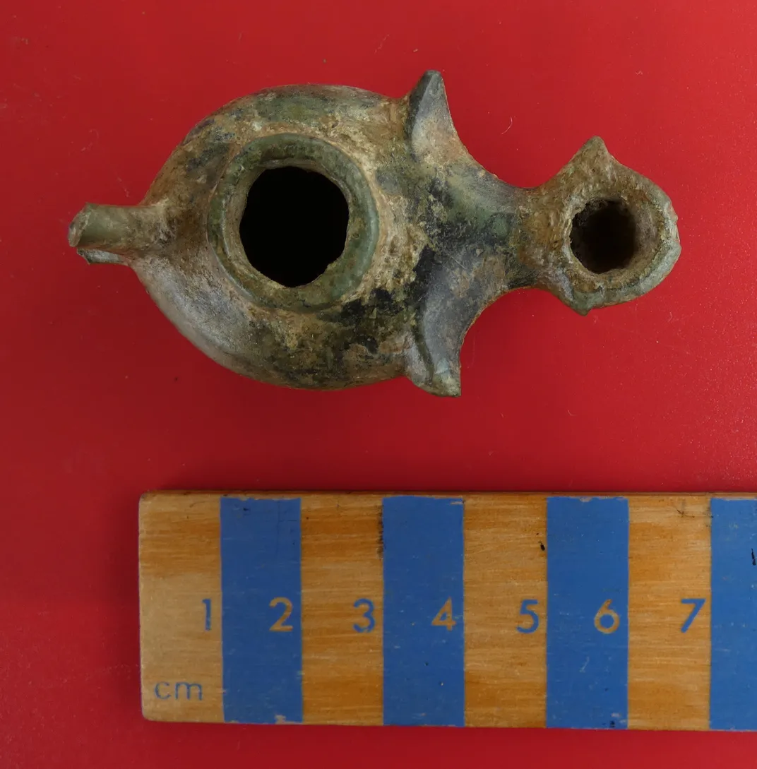 Overhead view of oil lamp artifact with measurement stick below