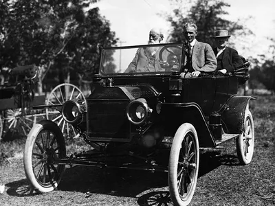 Henry Ford is at the wheel with John Burroughs and Thomas Edison seated in the back of a Model T.