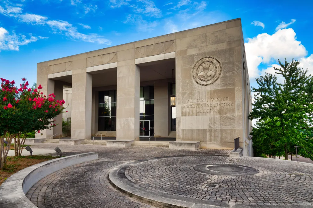 A view of a large brutalist building, with three large cement rectangular openings and glass windows
