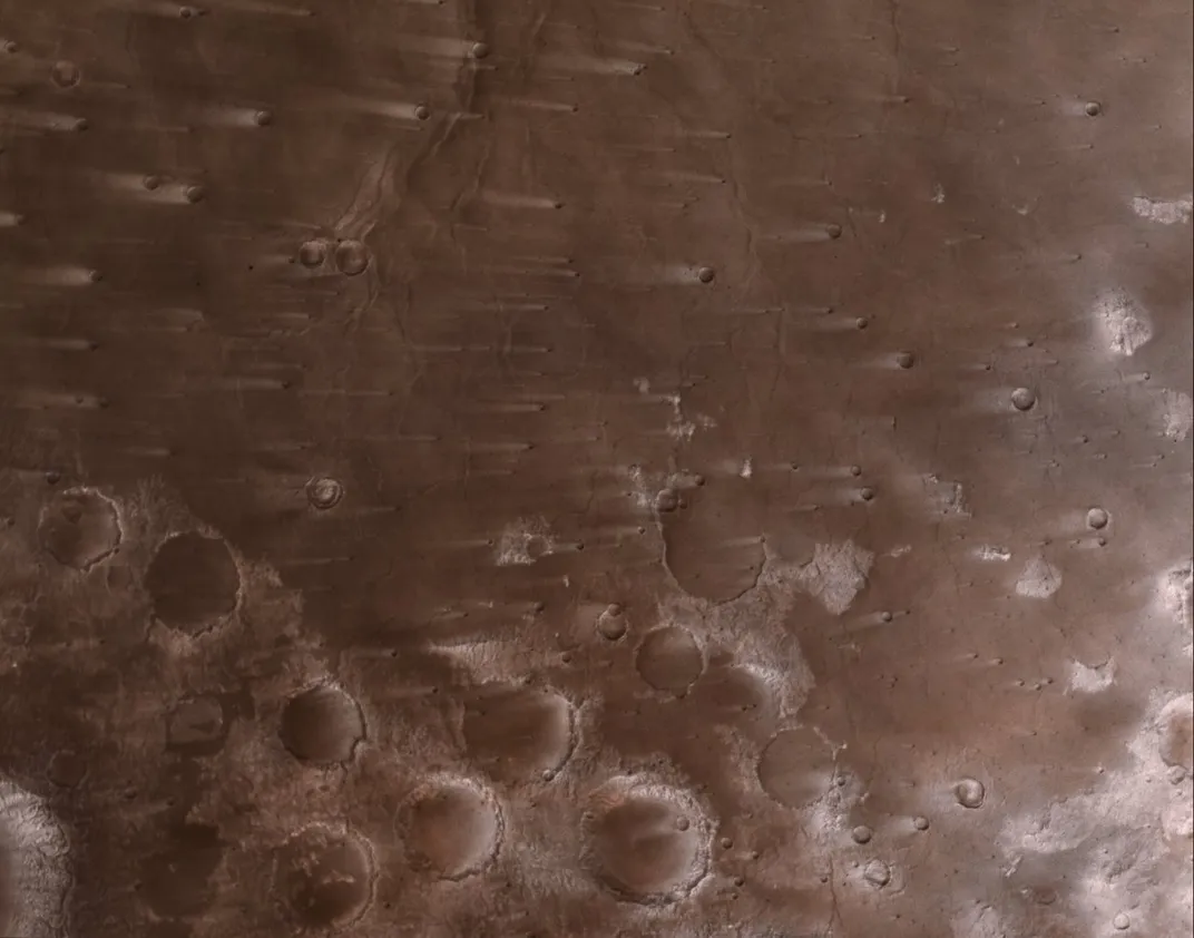 a cratered part of Mars with white streaks extending from some craters