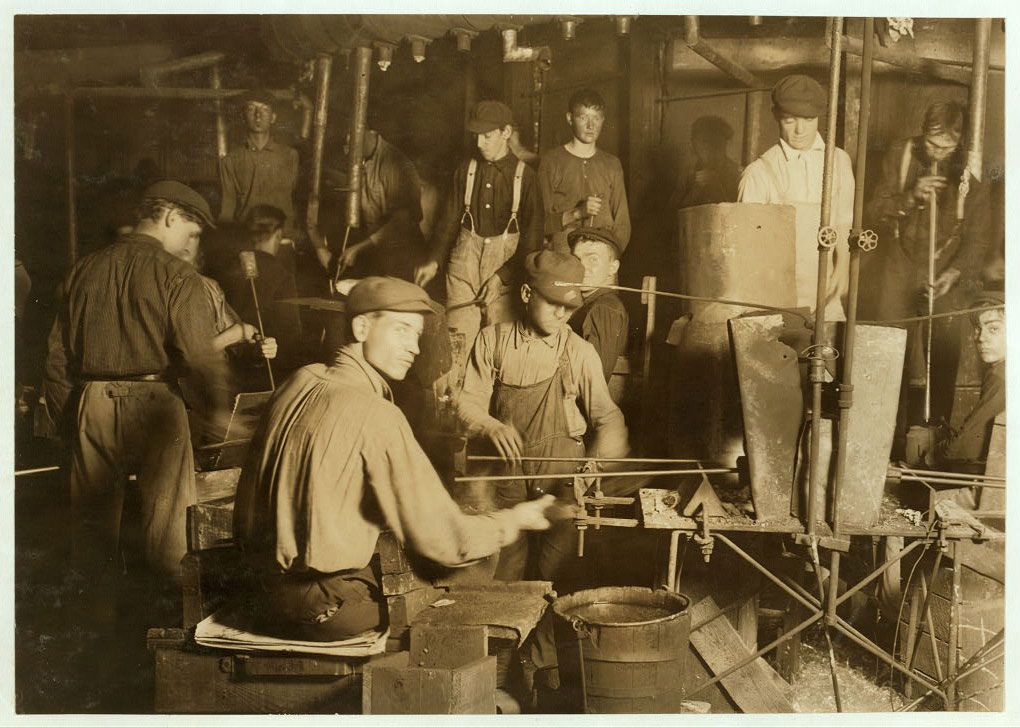 A group of men stand and sit among equipment in a low-ceilinged factory room. Black--and-white photo.