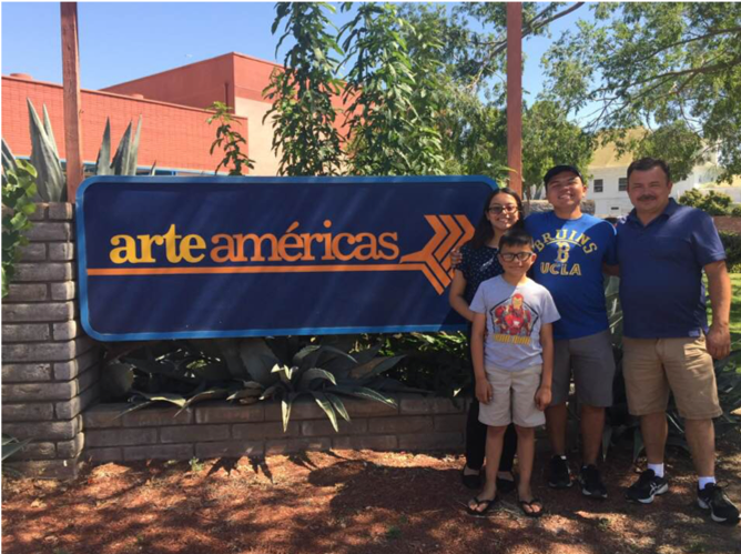 Image of Maya Castillo standing outdoors with three of her male family members next to the Arte Americas sign.