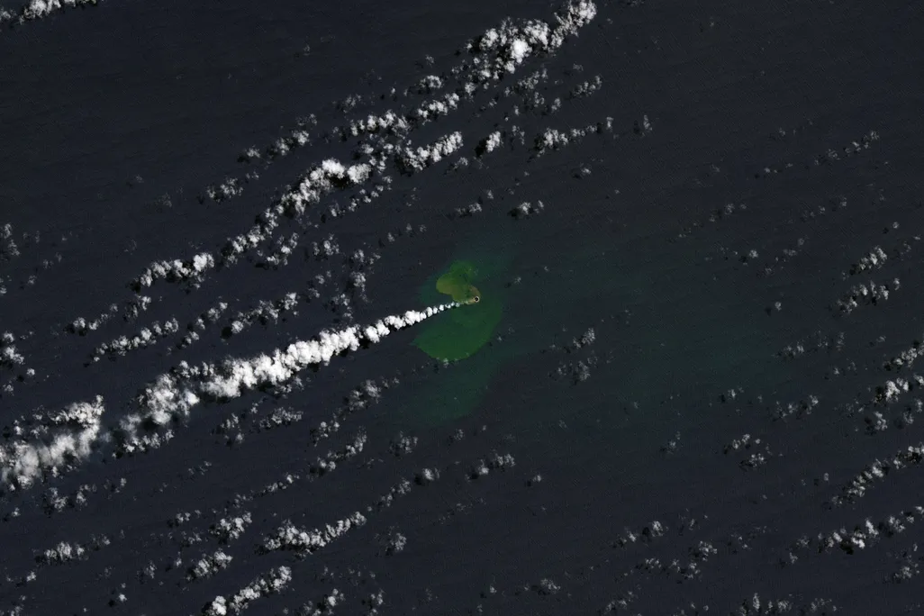 An aerial view of the Pacific Ocean shows a plume of ash from the recent eruption.