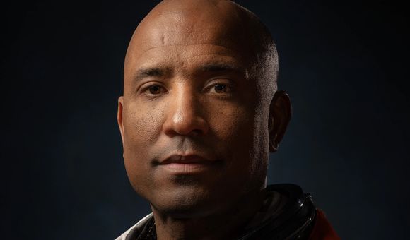 Dramatically-shot portrait of a Black male astronaut in an orange spacesuit.