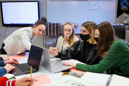 Peterson wears a bun and blazer pointing towards a computer screen with her students
