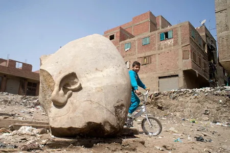 A boy rides his bike by the recently discovered statue that may be of Pharaoh Ramses II, one of the Egypt's most famous ancient rulers.