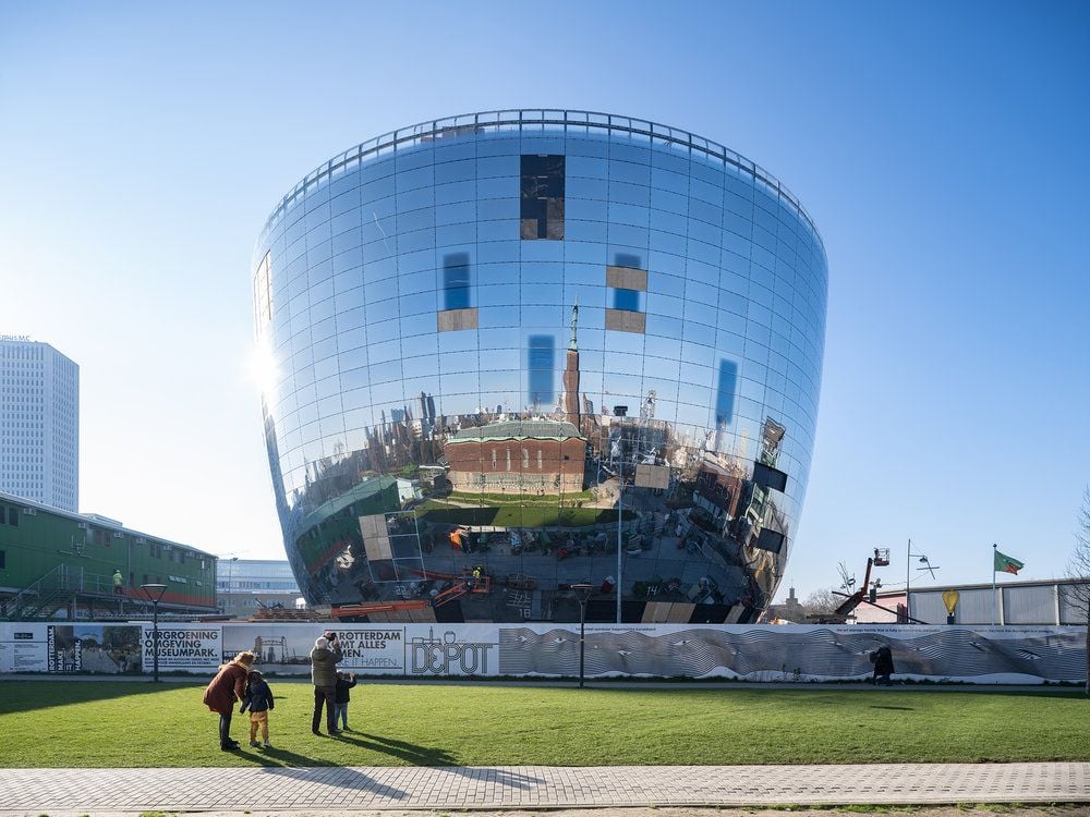A large building shaped like a sphere with a flat top, with mirrors all around the building's surface that reflect the blue sky and white clouds