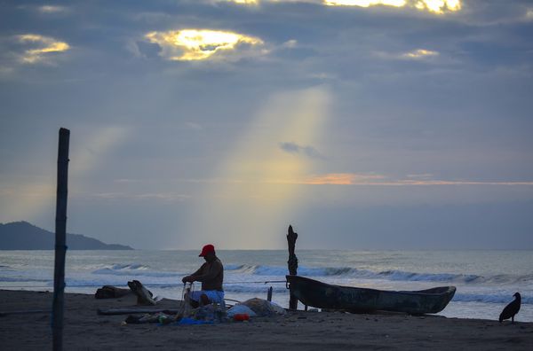 A fisherman mending his nets at sunset. thumbnail