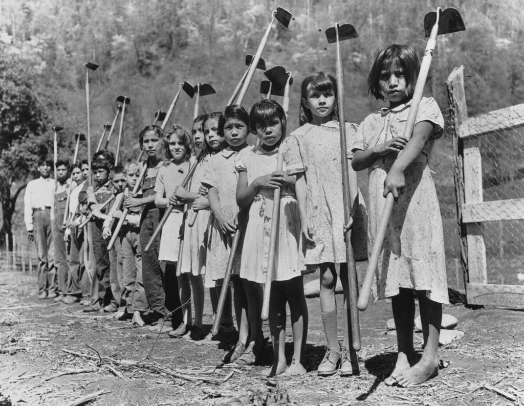 Black and white photo of children holding gardening tools