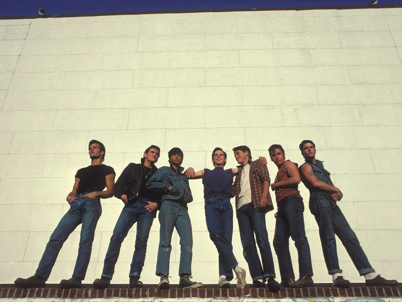The cast of The Outsiders pose in front of a brick wall