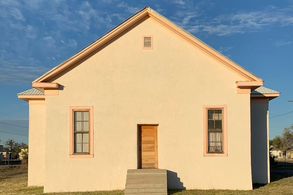 A front-on view of a simple white building with two windows on either side of a small door