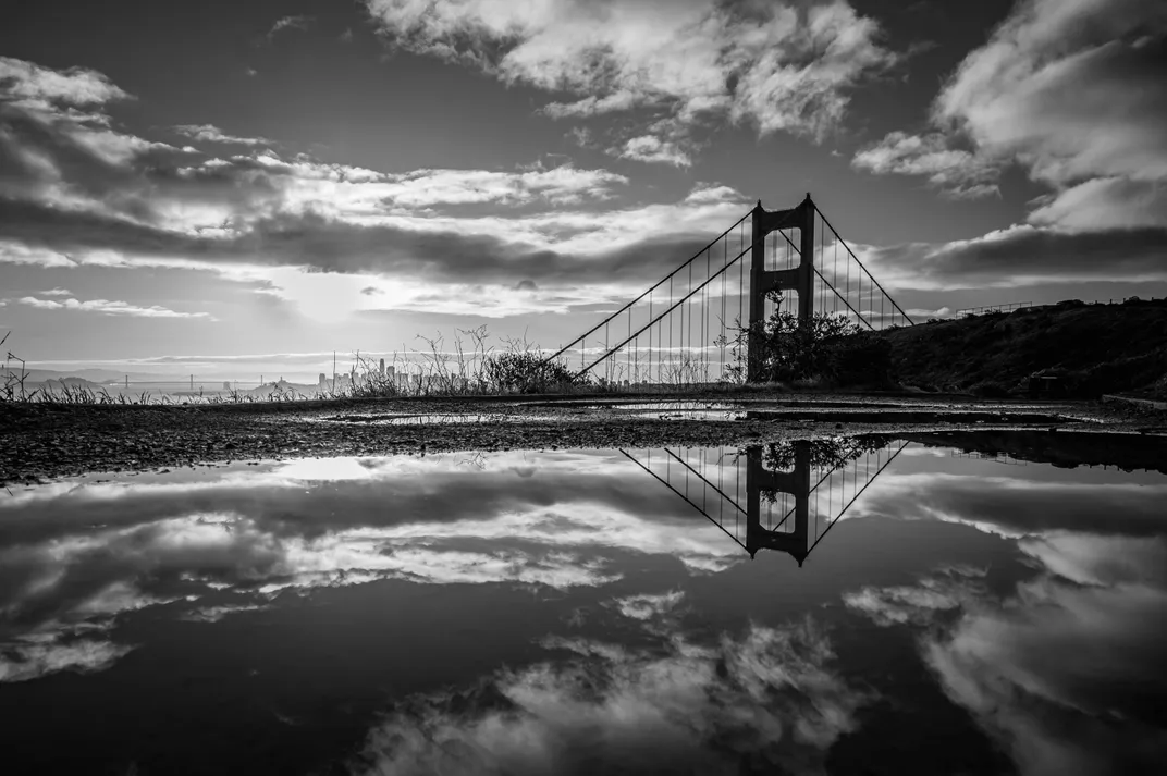 12 - A puddle reflects the Golden Gate Bridge and clouds, with the San Francisco skyline hidden in the background.