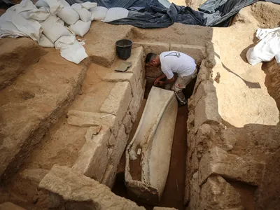 An archaeologist works on the second lead sarcophagus discovered, which is engraved with dolphins.