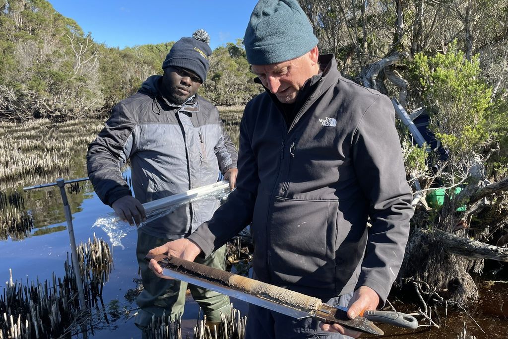 Two scientists study a sediment core in a swamp