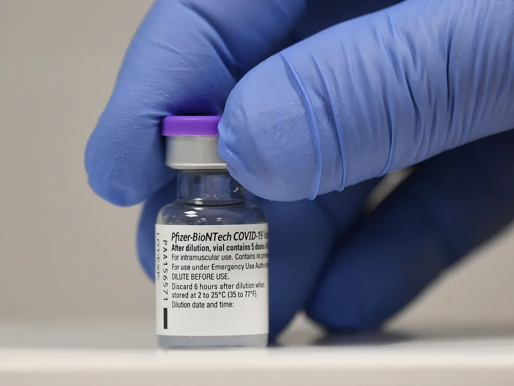 A vial of Pfizer's covid-19 vaccine being held by a gloved hand. 