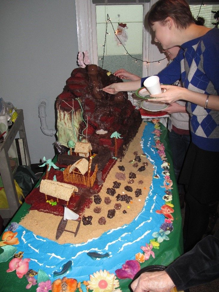 Brown volcano made of cake surrounded by an edible blue river and beige sand modeled after a volcano in Hawaii. 